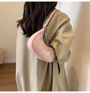 Sac demi-lune en jacquard rose porté en bandoulière sur un trench-coat élégant