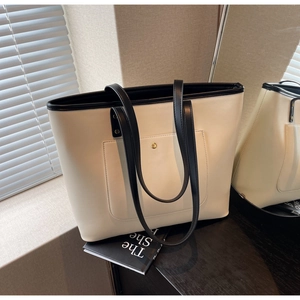 Detail of cream tote bag featuring black contrast trim and golden metal snap button
