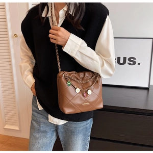 Détail du sac seau marron matelassé avec chaîne dorée et breloques décoratives
