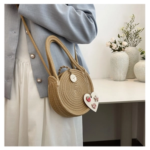 Detail of round straw crossbody bag with floral heart pendant and wooden button accent