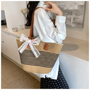 Close-up of straw tote bag featuring black stripes, lace bow, and floral embroidery
