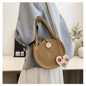 Detail view of woven straw beach bag featuring round wooden buckle and heart charm