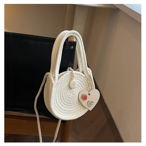 Detailed view of round white woven straw bag with spiral texture and heart charm