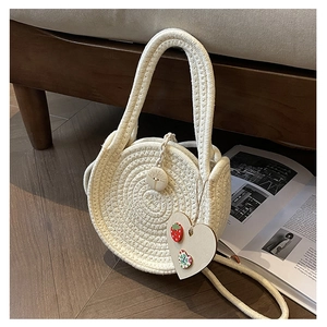 Detailed close-up of a round beige straw bag with heart pendant and floral embroidery