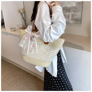 Detail of hand-woven straw tote bag with white lace bow and pink rose embroidery