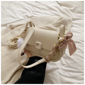 Detail of cream shoulder bag featuring silk scarf chain, plush ball, and leather strap