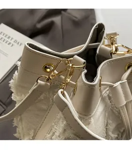 Detail of beige woven bucket bag featuring frayed edges and light gold metal hardware