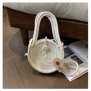 Detail of round white woven straw bag with rainbow stitching and wooden heart charm