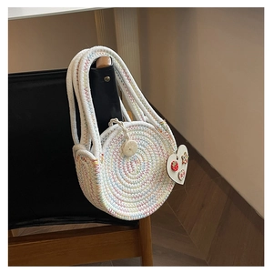 Detailed close-up of a circular woven straw bag featuring a strawberry heart pendant charm