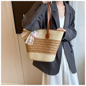 Detail of woven straw tote bag with brown leather handles and decorative lace bow charm