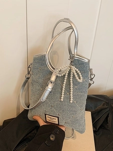 Sac à bandoulière en denim bleu clair avec strass et pendentif nœud en perles tenu en main
