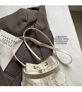 Detail of cream bucket bag with adjustable leather shoulder strap and gold hardware