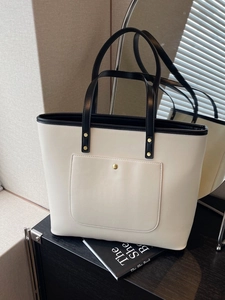 Minimalist beige tote bag with black handles and gold rivet detail on a wooden table