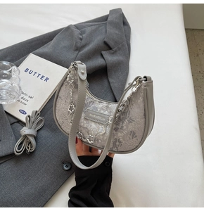 Détail du sac hobo en jacquard gris avec chaîne florale posé sur une veste grise