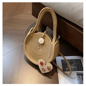 Detail of round straw bag showing heart-shaped strawberry charm and woven texture