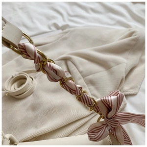 Close-up of golden chain strap with silk scarf detail and bow on cream leather bag