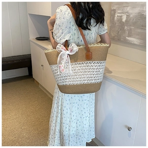Detail of straw woven tote bag featuring white lace bow and brown leather shoulder strap