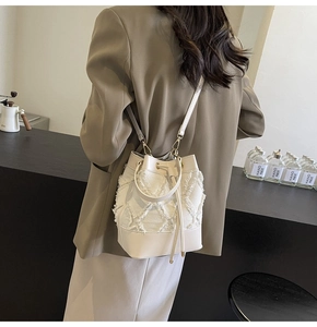 Detail of white denim quilted bucket bag with frayed edges and drawstring closure