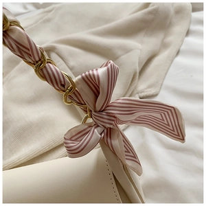 Detail of silk scarf intertwined with gold metal chain strap on beige leather handbag