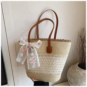 Detail of straw tote bag featuring white lace bow with pink rose embroidery and leather handles