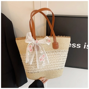 Detail view of woven straw tote bag featuring pink rose embroidery and white lace bow