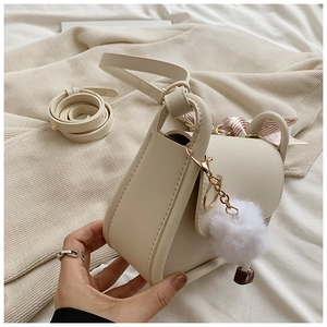 Detailed view of beige saddle bag with decorative scarf, fur pompom and long strap