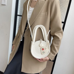 White woven circular crossbody bag with strawberry heart charm and dual handles