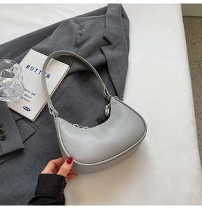 Détail du sac hobo gris clair avec chaîne en argent posé sur une veste minimaliste