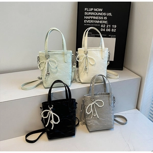Detailed view of four pleated mini bucket bags with pearl bows on a gray platform