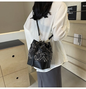 Detail of denim quilted bucket bag featuring frayed edges and black leather base on model