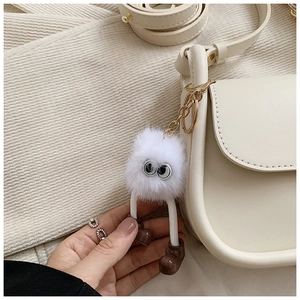 Close-up of a white fluffy monster charm with large eyes on a beige leather bag