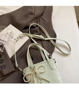 Detail of mint green bucket bag featuring a pearl bow charm and long shoulder strap