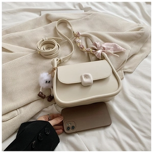 Close-up of a beige crossbody bag featuring a plush charm and striped scarf handle detail