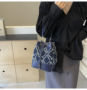 Detail of denim quilted bucket bag with fringe trim, gold hardware and drawstring closure