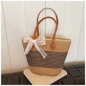 Detail of woven straw tote bag with black stripes, floral bow charm and lace trim