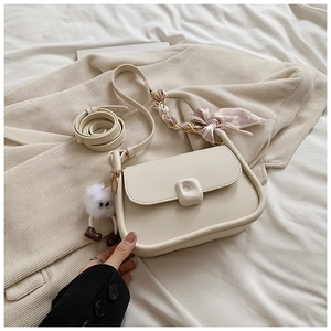 Detailed shot of cream curved flap bag with striped scarf chain and plush charm