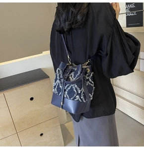 Detail of a denim bucket bag with white fringe quilting and drawstring closure worn by model