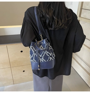 Detail view of denim bucket bag with frayed V-pattern and leather handle shown on model