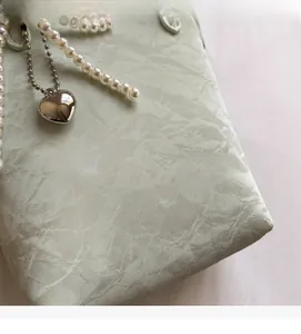 Detail of mint green PU bucket bag featuring pearl handle and heart metal pendant