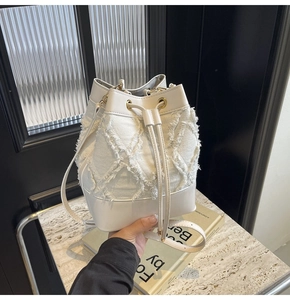 Macro shot of white denim bucket bag featuring frayed diamond texture and leather base
