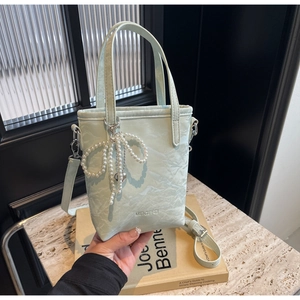 Detail of mint green ruched leather bucket bag featuring a pearl bow chain and logo