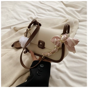 Detail view of cream saddle bag with brown trim and colorful scarf keychain charm