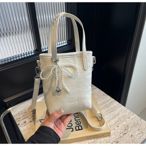 Detail of white bucket bag featuring pearl bow charm and silver heart pendant detail