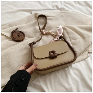 Detail of minimalist beige crossbody bag featuring brown contrast piping and silk scarf decor