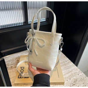 Detail of creamy white bucket bag with pearl bow accessory and black enamel heart