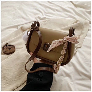 Detail of a brown flap crossbody bag with scarf-wrapped chain handle and plush charm