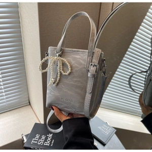Detail of light gray textured bucket bag with pearl bow charm and modern double handles