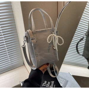 Detail of light gray textured bucket bag with pearl bow charm and silver hardware accents