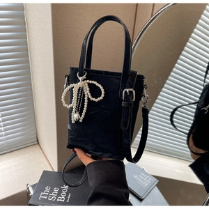Detail of black tote bag featuring textured fabric and pearl bow charm with metal heart