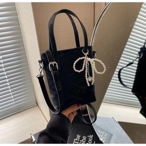 Close-up of black suede mini bucket bag featuring a delicate pearl bow charm and dual straps